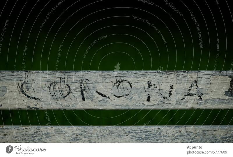 Verblassender Schriftzug "CORONA" in schwarzen Großbuchstaben auf einer weißen Holzbank vor unscharfem dunklem Hintergrund Corona Lettern verblassen Parkbank