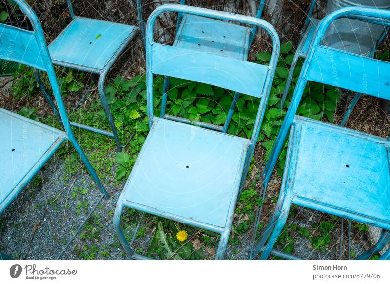 identische, blaue Stühle stehen im Halbschatten auf teilweise von grünen Blättern überdecktem Schotter nebeneinander Vorrat stabil Sitzgelegenheit Patina