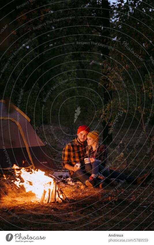 Ein junges Pärchen, ein Mann und ein Mädchen mit hellen Strickmützen, hielt an einem Camping Paar Typ Vollbart Hüte gestrickt Wärme Zelt Freudenfeuer Liebe