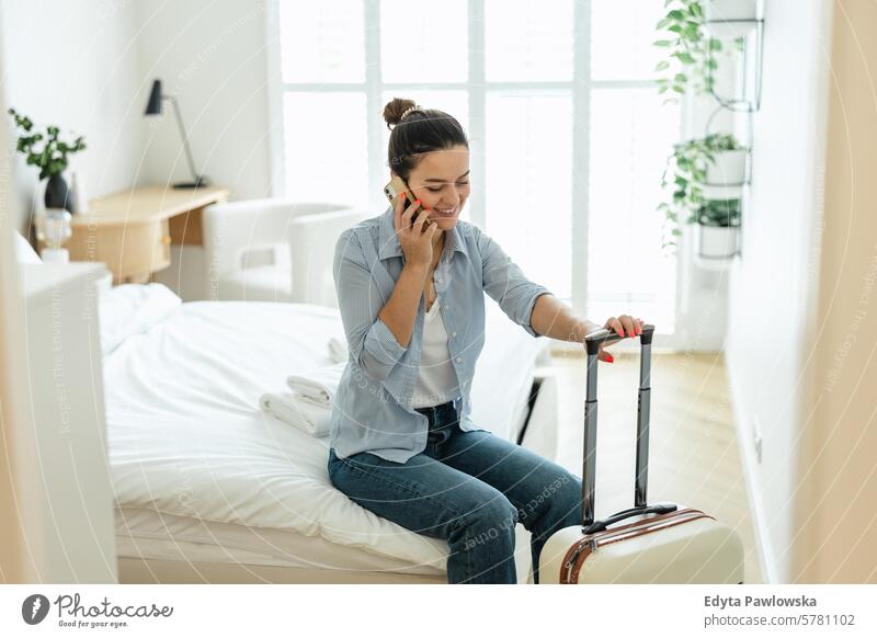 Junge Frau mit einem Koffer sitzt auf dem Bett in einem Hotelzimmer und telefoniert Verpackung Bekleidung Ferien reisen Vorbereitung Menschen Gepäck eine Person