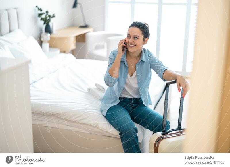 Junge Frau mit einem Koffer sitzt auf dem Bett in einem Hotelzimmer und telefoniert Verpackung Bekleidung Ferien reisen Vorbereitung Menschen Gepäck eine Person