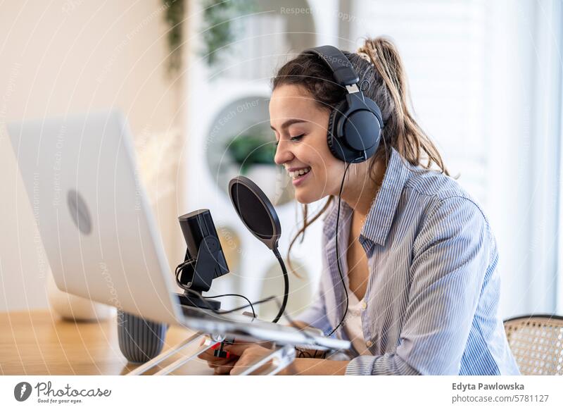 Frau mit Kopfhörern, die an einem Schreibtisch sitzt und in ein Mikrofon spricht und einen Podcast aufnimmt Menschen eine Person Raum Wohnzimmer Erwachsener