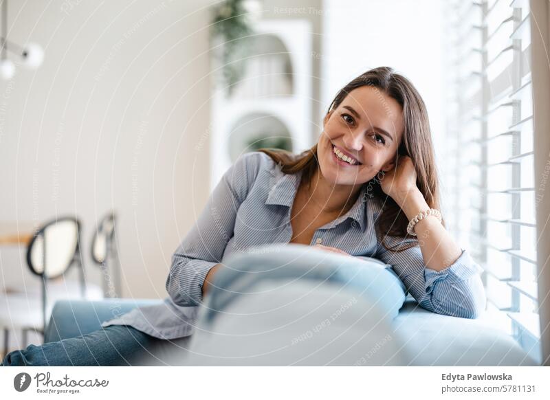 Porträt einer lächelnden jungen Frau, die zu Hause auf dem Sofa sitzt Menschen eine Person Raum Wohnzimmer Erwachsener junger Erwachsener im Innenbereich