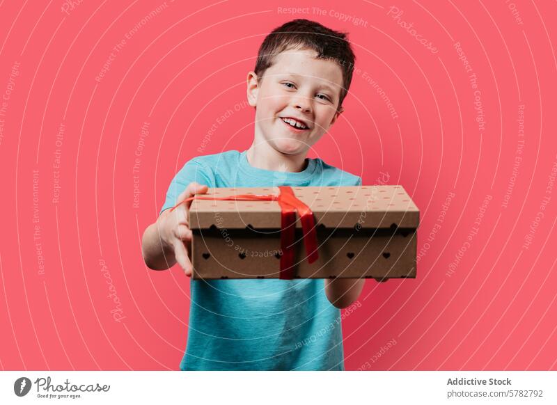Glücklicher Junge präsentiert eine Geschenkbox auf rosa Hintergrund präsentieren Kasten Bändchen Lächeln Kind rot Punktmuster Freude freizügig Feier festlich