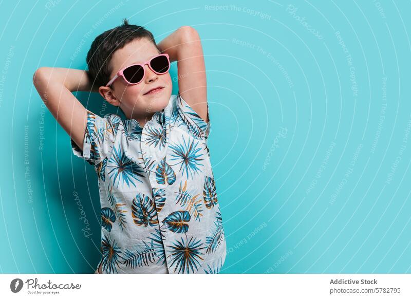 Junge in Tropenhemd und Sonnenbrille beim Entspannen Kind jung Erholung lässig rosa Freizeit heiter Glück Hände hinter dem Kopf türkisfarbener Hintergrund cool