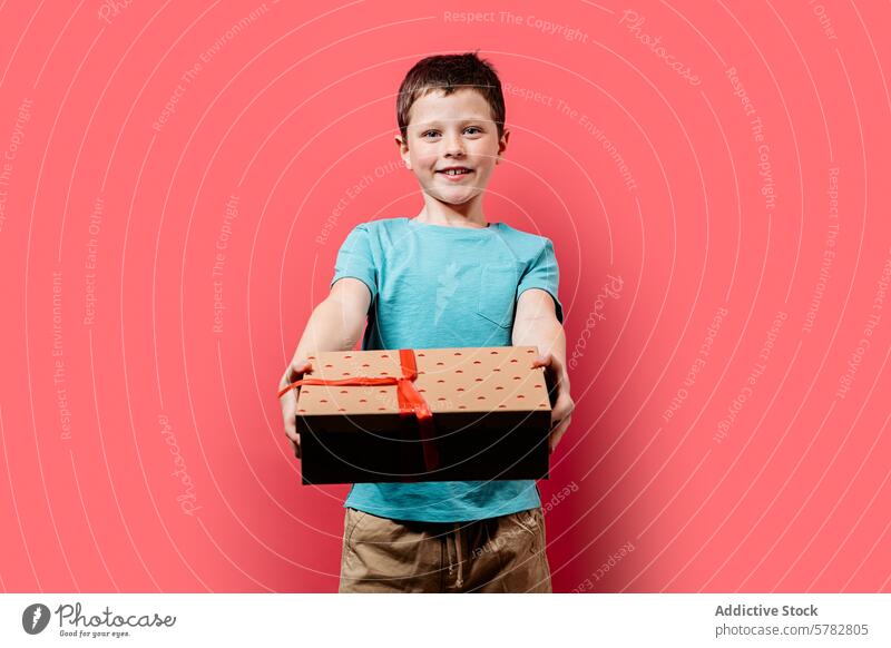 Glückliches Kind präsentiert eine Geschenkbox auf rosa Hintergrund präsentieren Kasten Lächeln Junge pulsierend jung Beteiligung eingewickelt heiter Geben