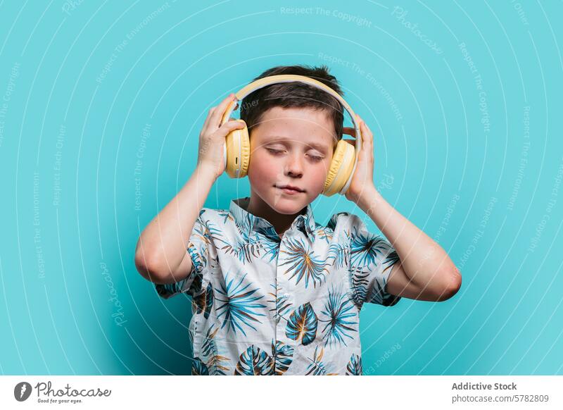 Junge genießt Musik mit gelben Kopfhörern Blauer Hintergrund Blumenhemd hören Genuss Kind Freizeit Audio Klang geschlossene Augen Gefühl jung Windstille