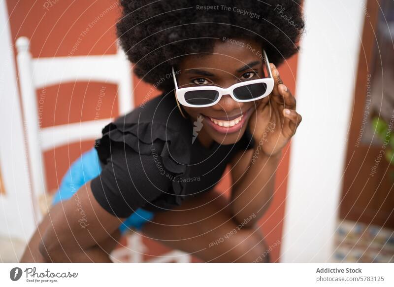 Lebhaftes Lächeln einer jungen Afro-Frau mit modischer Sonnenbrille Afrikanisch Afro-Look Frisur heiter stylisch weiß Mode freudig Lifestyle spielerisch