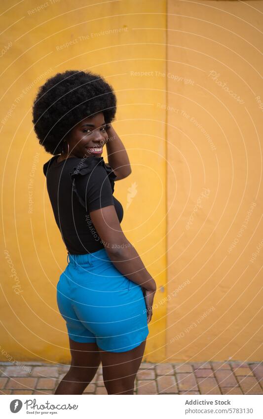 Porträt einer lebendigen, urbanen, modischen Afro-Frau Mode Stil heiter selbstbewusst hell gelb Wand schick trendy stylisch Pose pulsierend jung Erwachsener