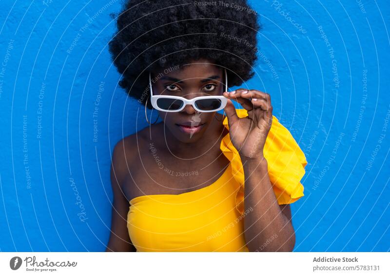 Stylish Afro Frau Posing gegen blaue Wand Afro-Look Lifestyle Mode Selbstvertrauen Pose gelb Kleid weiß Sonnenbrille Hintergrund pulsierend schick stylisch