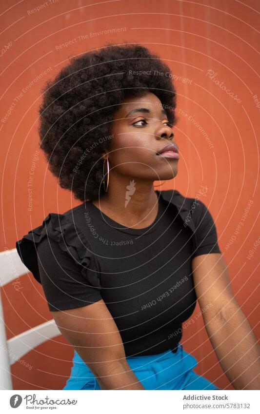 Kontemplative Afro-Frau in Freizeitkleidung Afro-Look beschaulich Starrer Blick Entfernung schwarze Spitze blaue Hosen oranger Hintergrund jung nachdenklich