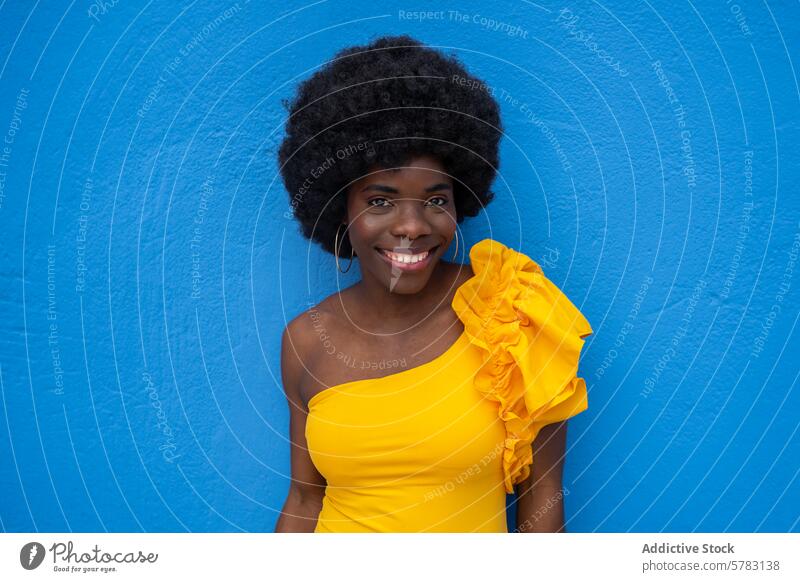 Lächelnde Frau in Gelb mit blauem Hintergrund Afro-Look gelbes Kleid Blauer Hintergrund pulsierend freudig Glück Mode Lifestyle Porträt Behaarung Afrikanisch