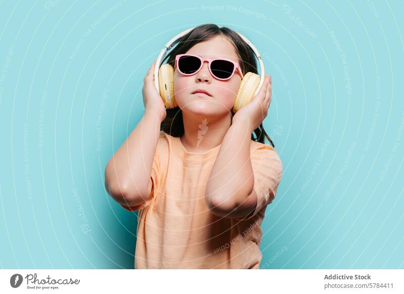 Junges Mädchen genießt Musik mit Kopfhörern und Sonnenbrille türkisfarbener Hintergrund Spaß Stil hören jung Kind rosa gelb Genuss Audio Freizeit Entertainment