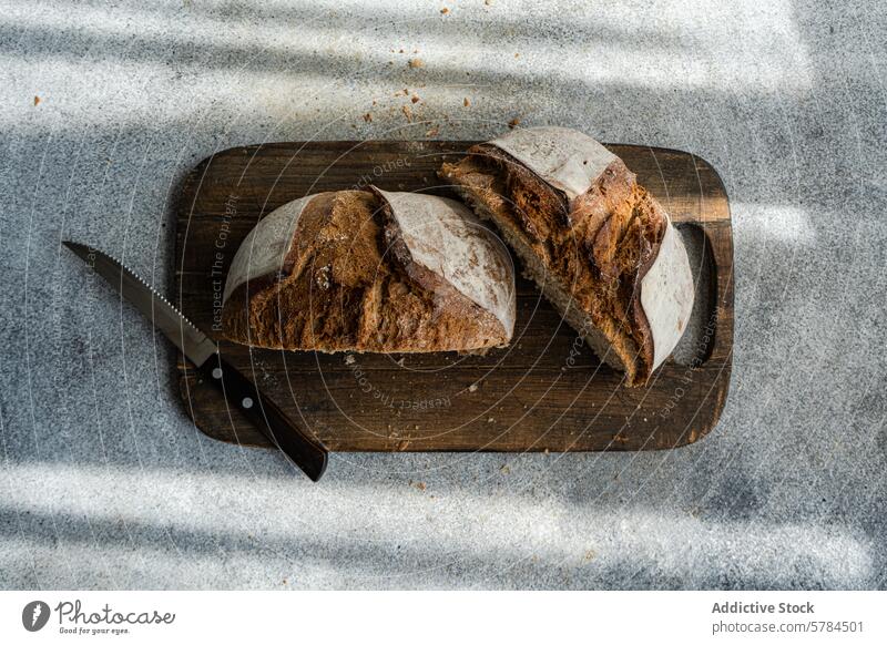 Handwerkliches Roggen-Sauerteigbrot auf Holzbrett Brot Gesundheit aufgeschnitten hölzern Schneidebrett verzahnt Messer Schatten Licht rustikal heilsam natürlich
