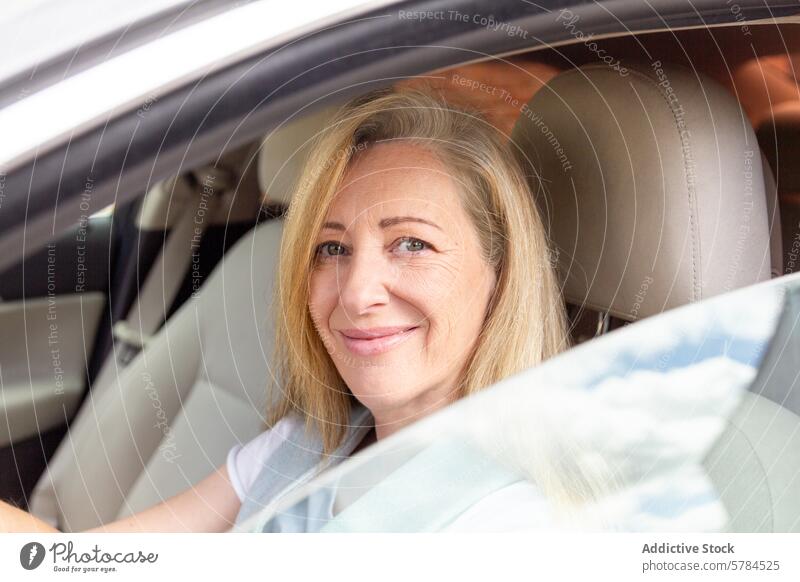 Reife Frau lächelnd im Auto sitzend reif Lächeln PKW fahren Fahrer Sitz blond Behaarung heiter Fotokamera Fenster Fahrzeug Erwachsener Verkehr Transport
