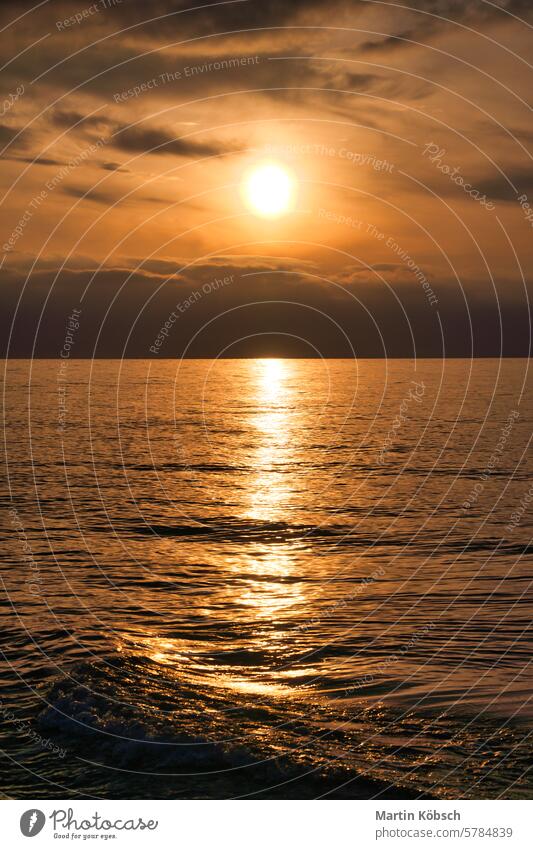 Sonnenuntergang, beleuchtetes Meer. Ein paar Wolken am Himmel, leichte Wellen rollen an den Strand Sonnenstrahlen Sonnenschein Reflexion & Spiegelung Ostsee