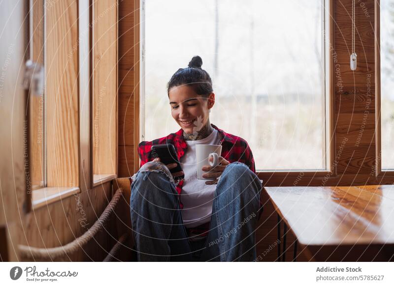 Gemütliche Wohnumgebung mit einer Frau, die ihr Smartphone und ihren Kaffee genießt Lächeln Fenster Komfort Erholung heimwärts sonnendurchfluteter Raum Sitzen
