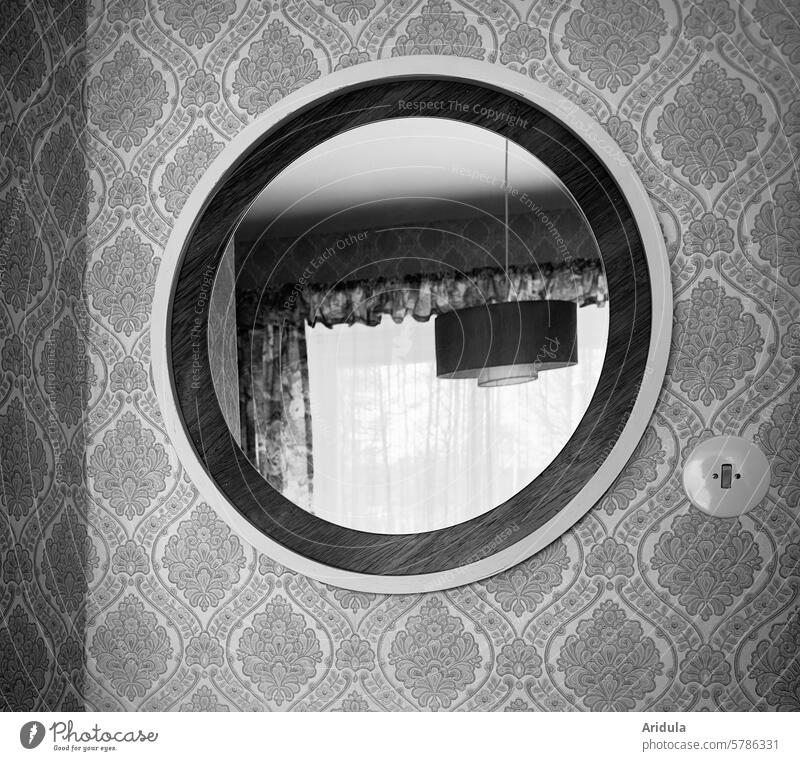 50er | alter runder Spiegel hängt an einer gemusterten Wand | in dem Spiegel spiegelt sich eine Deckenlampe und ein Fenster mit Vorhängen 50er Jahre retro