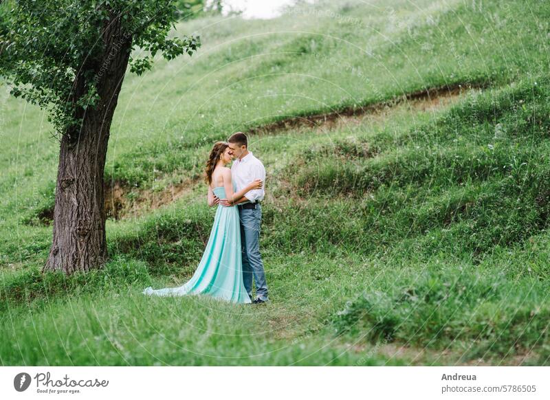 glücklicher Kerl in einem weißen Hemd und ein Mädchen in einem türkisfarbenen Kleid gehen im Waldpark jung Glück Gras Bäume Sträucher Park grün braun