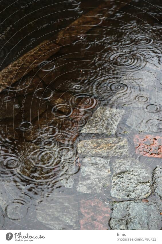großzügige Spülung Regen Regentropen Regenwasser nass feucht überschwemmt Straße Kopfsteinpflaster Fahrbahnrand Bürgersteig Ringe Überschwemmung Element