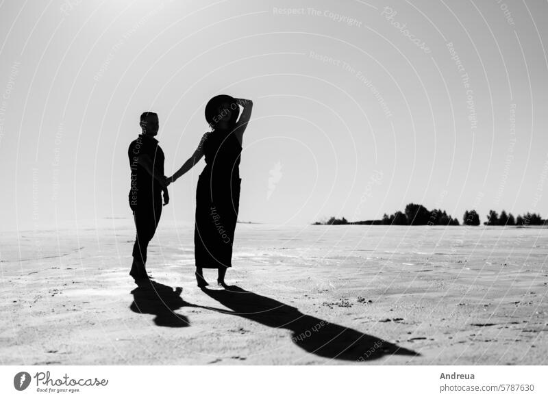 junges Paar ein Kerl und ein Mädchen mit freudigen Emotionen in schwarzer Kleidung gehen durch die weiße Wüste Barfuß blau Tag Fußspuren Freiheit Spaß Typ Hut