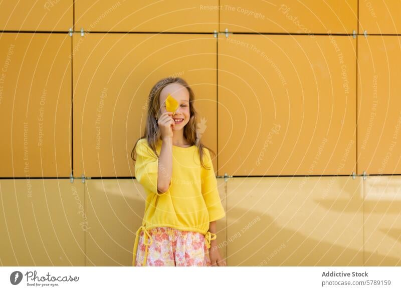 Junges Mädchen spielt mit einem Blatt in Herbstfarben Kind spielerisch gelb Glück Lächeln Wand hell Stehen Outfit niedlich Freude Spaß lässig Saison heiter