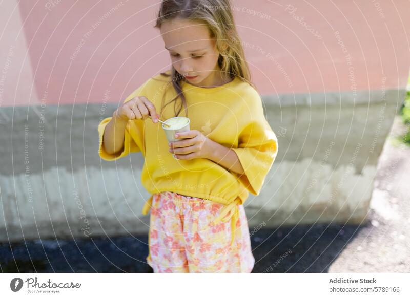Junges Mädchen genießt Eiscreme an einem sonnigen Tag jung Kind Speiseeis Essen blondes Haar gelber Pullover Blümchenhose Stehen Sommer Snack Leckerbissen
