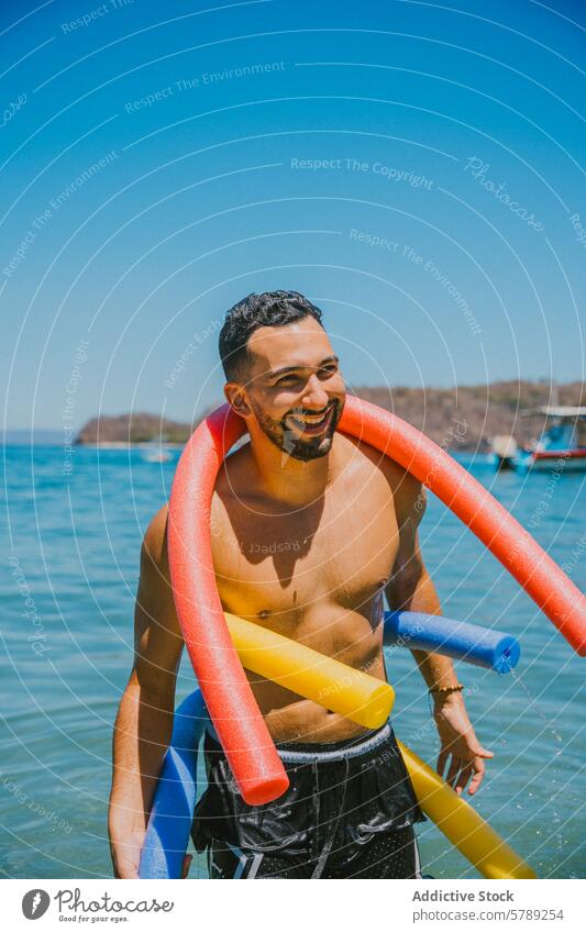 Lächelnder Mann spielt mit bunten Poolnudeln am Strand spielen Wasser tropisch Freizeit Freude Gleichgewicht pulsierend Farbe sonnenbeschienen Costa Rica Küste