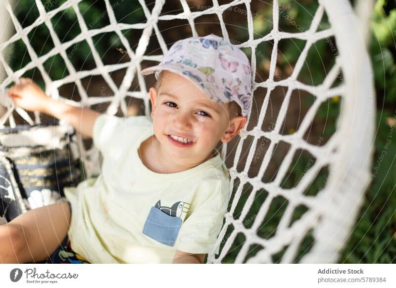 Fröhliches Kind spielt auf einer Schaukel im Garten pendeln spielen Freude Lächeln Verschlussdeckel im Freien sonnig heiter jung Sitzen weiß Genuss Spaß
