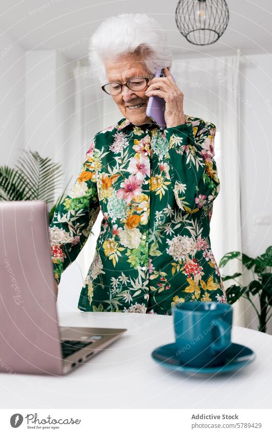 Ältere Frau beim Multitasking zu Hause mit Technik Senior älter heimwärts arbeiten Technik & Technologie Laptop Telefon Gespräch Bluse geblümt Innenbereich