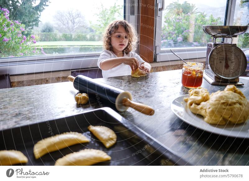 Kleines Kind beim Backen in einer Küche mit Nudelholz und Teig backen Teigwaren Gebäck Kneten Konzentration krause Haare sonnig heimwärts Essen zubereiten