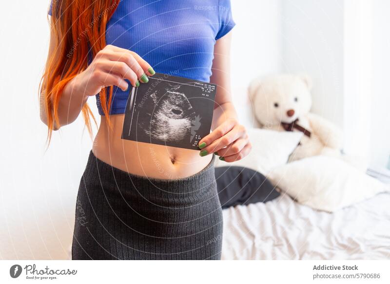 Werdende Mutter hält Ultraschallbild mit Teddybär im Hintergrund Schwangerschaft Mutterschaft erwartungsvoll Frau jung Baby Scan Beteiligung Raum gemütlich Bett