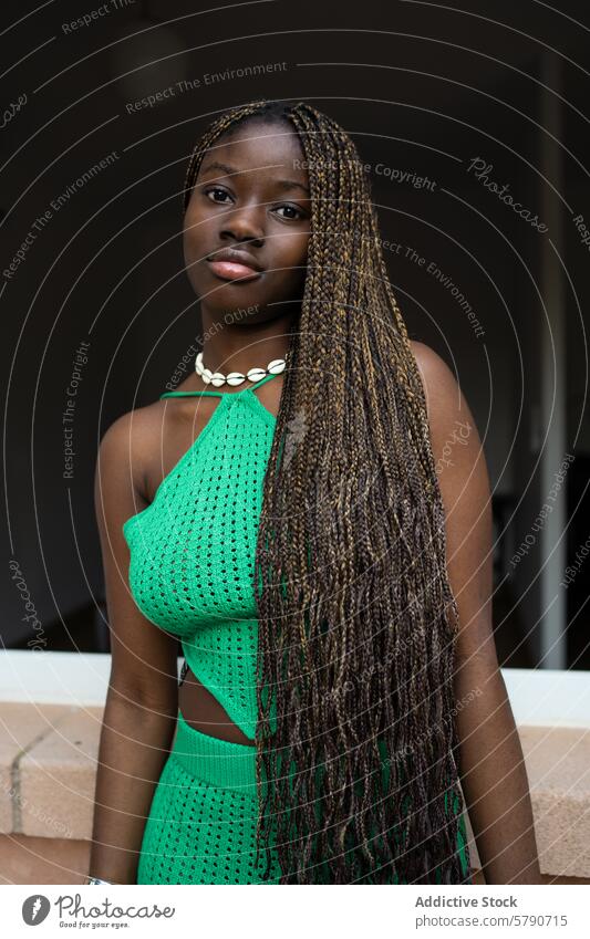 Eine selbstbewusste junge Schwarze mit kunstvollen Zöpfen trägt ein leuchtend grünes Häkelkleid, das Selbstvertrauen und Stil ausstrahlt Frau schwarz Zopf Mode