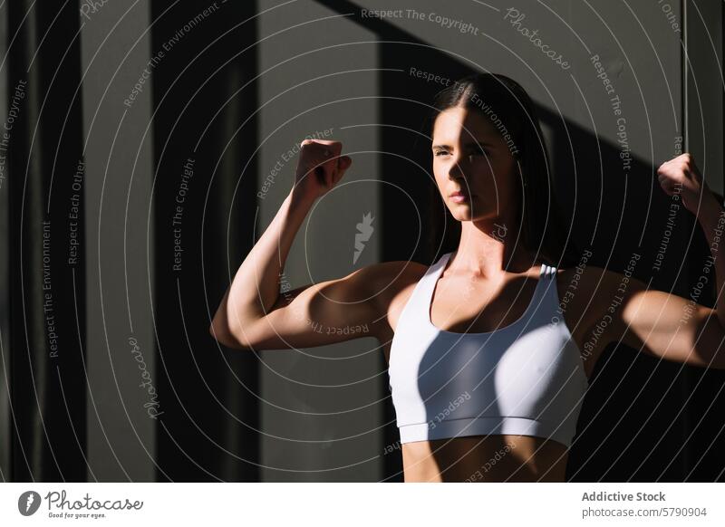 Sportliche Frau demonstriert Stärke zu Hause Athlet Fitness Sportbekleidung Muskel flex Sonnenlicht Schatten heimwärts selbstbewusst Gesundheit Training Körper