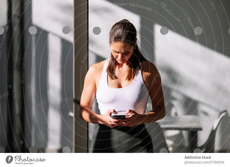 Fitte Frau telefoniert in einer modernen Wohnumgebung Athlet Smartphone heimwärts Lifestyle Gesundheit Fitness Raum sonnenbeschienen fokussiert sportlich