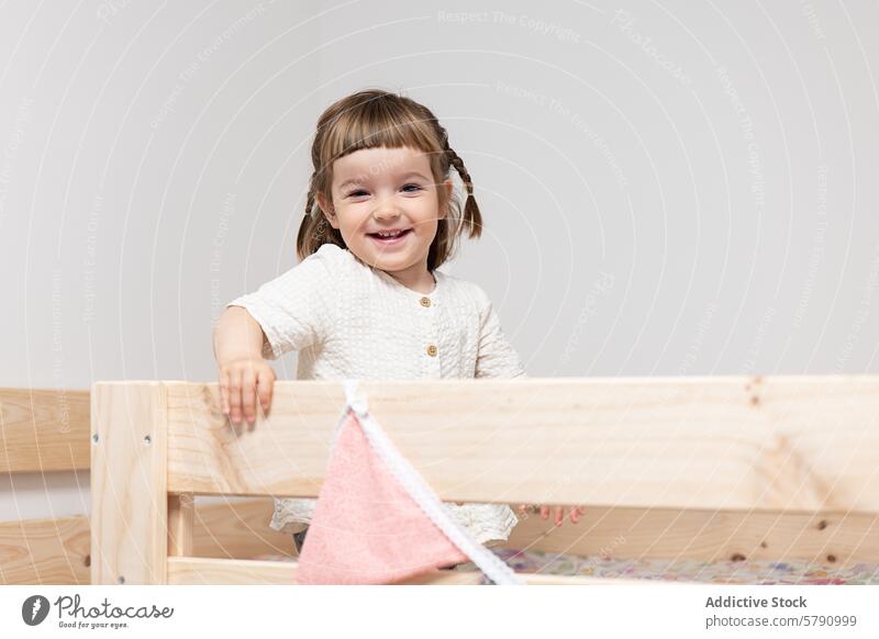Glückliches Kleinkind-Mädchen spielt in einem Holzbett Bett hölzern Lächeln spielen Kind Zöpfe heiter Stehen Schlafzimmer Möbel Decke weich Gewebe