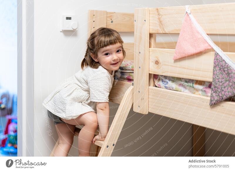 Kind klettert mit einem spielerischen Lächeln auf ein Etagenbett aus Holz Mädchen Klettern Laufmasche hölzern Raum Sauberkeit hell heiter Glück im Innenbereich