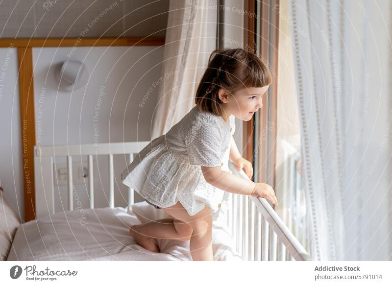 Junges Mädchen im weißen Kleid schaut aus dem Fenster Kind Schlafzimmer neugierig Bett im Innenbereich heimwärts Blick Stehen hell Raum heimisch Morgen Licht