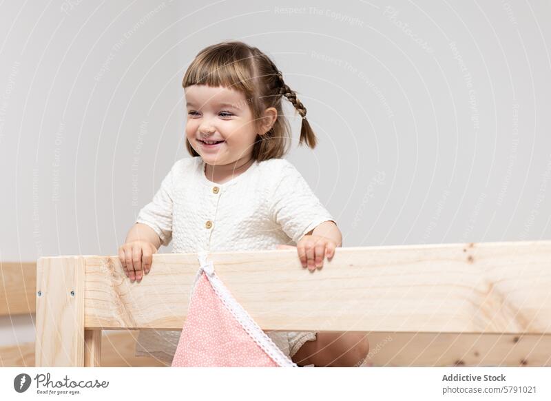 Lächelndes Kleinkind-Mädchen lehnt sich an Holzmöbel Glück Möbel Unschuld Freude Kind Geflecht Behaarung fettarm Struktur spielerisch niedlich im Innenbereich