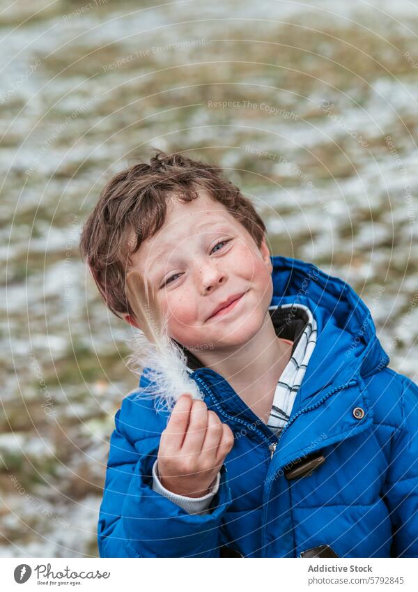 Lächelnder Junge im Freien, der eine Feder hält Kindheit Fröhlichkeit Freizeit spielen Spaß Familie Tag Jacke blau Winter kalt krause Haare heiter spielerisch