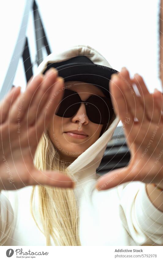 Stylische blonde Frau posiert mit Sonnenbrille und Kapuze Straße Stil Mode Kapuzenpulli posierend Rahmen Gesicht Hand urban Großstadt Jugend Accessoire lässig