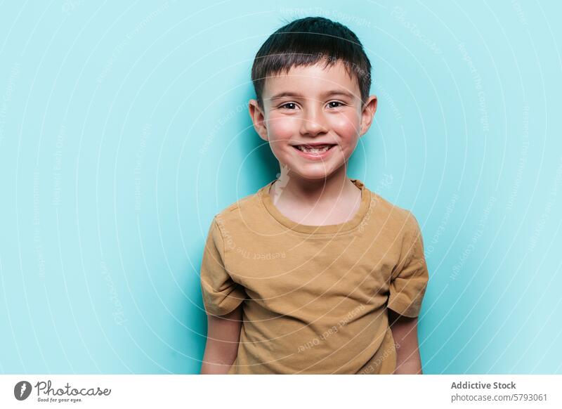 Fröhlicher Junge lächelt in einer Studioumgebung Kind Lächeln Porträt Atelier Glück Freude Blauer Hintergrund Unschuld männlich heiter Ausdruck positiv Jugend