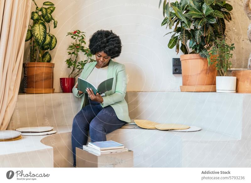 Eine Frau liest in einem modernen Coworking Space lesen Buch Raum Afroamerikaner Pflanze stylisch Möbel gut beleuchtet Fokus im Innenbereich sitzend