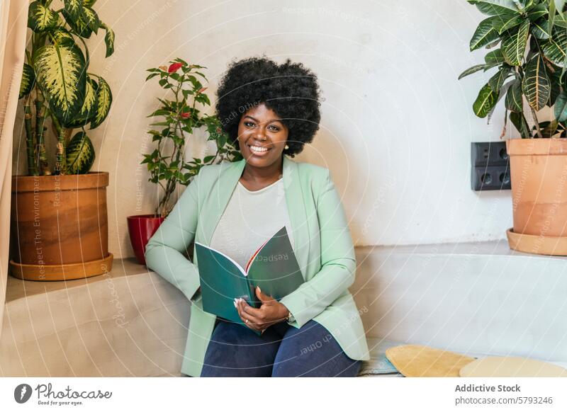 Lächelnde berufstätige Frau im grünen Blazer mit einem Notebook professionell Grüner Blazer sitzend Zimmerpflanzen Coworking Space Stil Selbstvertrauen