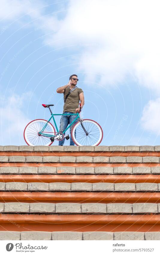 Mann mit Fahrrad auf dem Dach ruft an Dachterrasse Aufruf Telefon Himmel urban Lifestyle Konnektivität selbstbewusst Mobile Mitteilung Freizeit im Freien