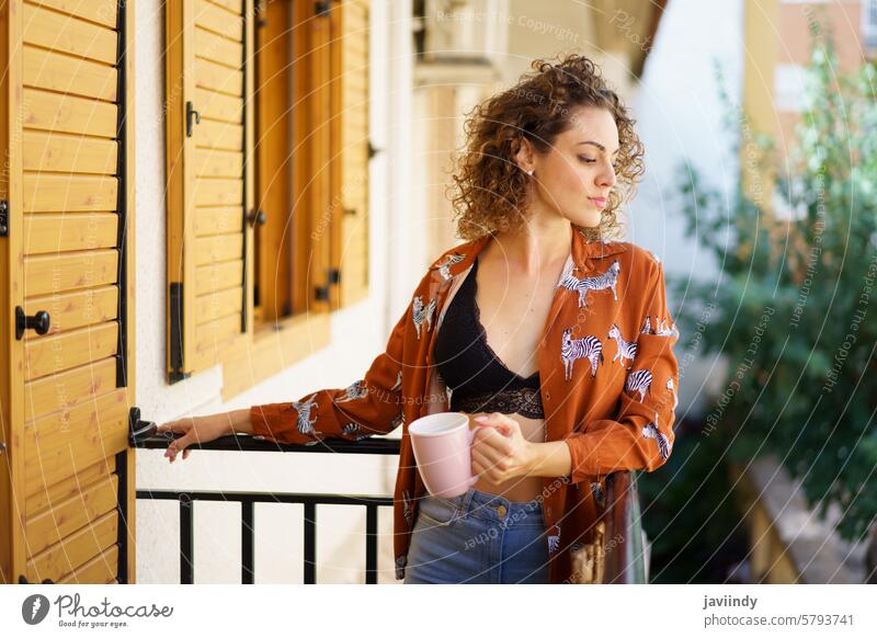 Junge Frau steht mit einer Tasse Kaffee auf dem Balkon lässig Terrasse trinken Getränk krause Haare Windstille friedlich Dame verträumt allein Heißgetränk