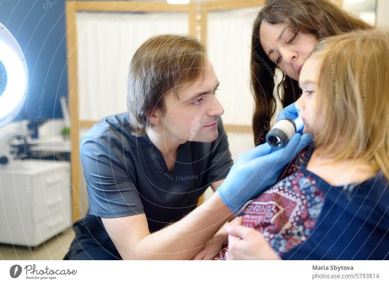 Ein fürsorglicher Arzt untersucht Muttermale auf der Haut eines kleinen Kindes. Ein Dermatologe betrachtet einen Ausschlag am Hals eines Mädchens mit einem Dermatoskop. Baby bei einem Termin beim Kinderarzt