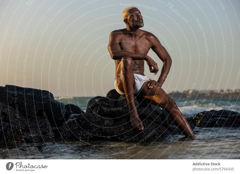 Afrikanisches amerikanisches männliches Modell posiert auf Strandfelsen in der Abenddämmerung Afroamerikaner Steine Meer Gelassenheit posierend Gedanke ethnisch