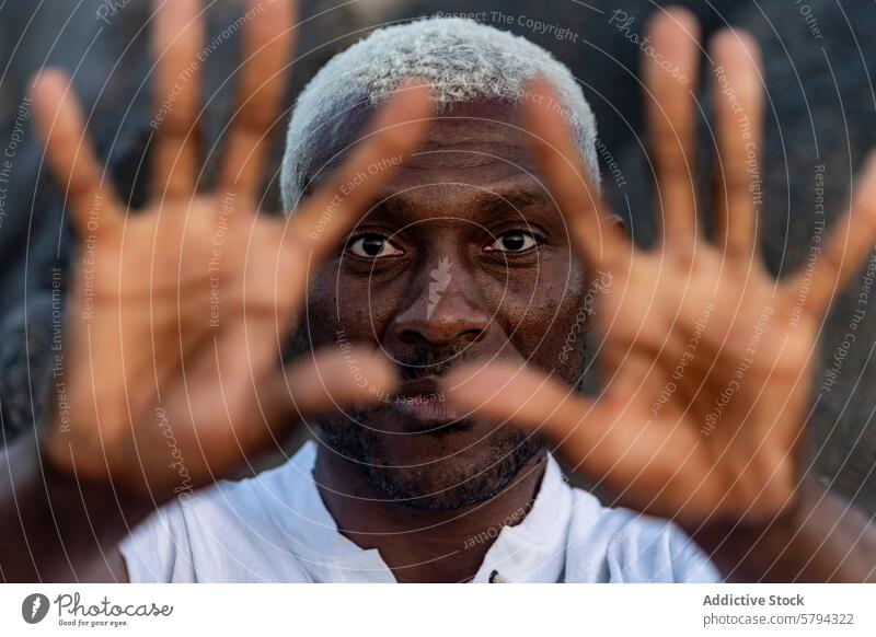 Ein fesselndes Nahaufnahme-Porträt eines afroamerikanischen Mannes mit auffallend weißem Haar, der durch seine ausgestreckten Finger blickt Afroamerikaner