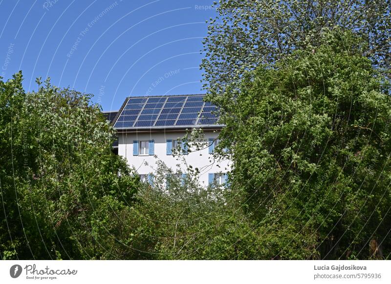 Installation von Solar- oder Fotovoltaikanlagen auf dem Dach eines Einfamilienhauses, beobachtet an einem sonnigen Tag in einem Schweizer Dorf. Um das Haus herum gibt es Bäume und Büsche.